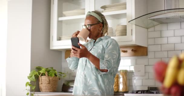 Una Mujer Afroamericana Mayor Bebe Café Lee Teléfono Inteligente Cocina — Vídeo de stock
