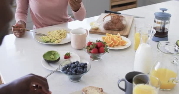 非洲裔美国人夫妇在厨房里享受着健康的早餐 她手里拿着一只勺子 桌上放着新鲜的水果和炒鸡蛋 毫发无损 动作缓慢 — 图库视频影像