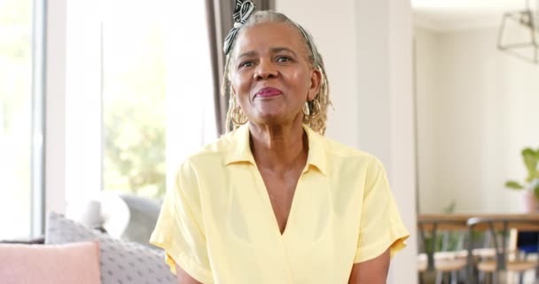 一位非洲裔美国老年妇女在视频通话中 穿着黄色衣服 笑容满面 她的欢乐弥漫在明亮舒适的客厅里 反映出舒适 时尚的家 没有变化 动作缓慢 — 图库视频影像