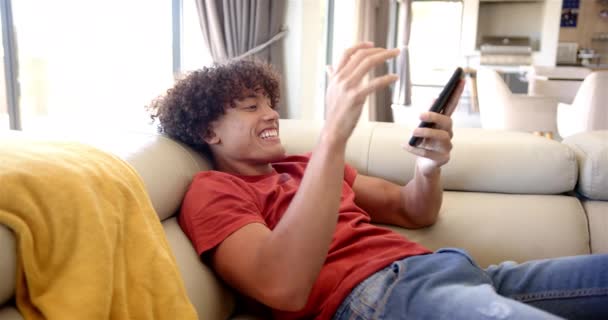 Młody Dwurasowy Mężczyzna Wypoczywa Kanapie Domu Smartfonem Ręku Kręcone Włosy — Wideo stockowe