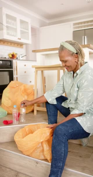 自宅でリサイクルするアフリカ系アメリカ人女性 彼女は灰色の髪をしていて 軽いシャツを着ていて 彼女の手にあるアイテムに焦点を当てています — ストック動画