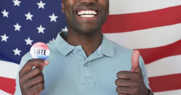 陽気なアフリカ系アメリカ人男性が有権者バッジを見せている 彼は明るい笑顔 短い黒い髪を持っており 軽いブルーポロシャツを着ています 変更されていない スローモーション — ストック動画