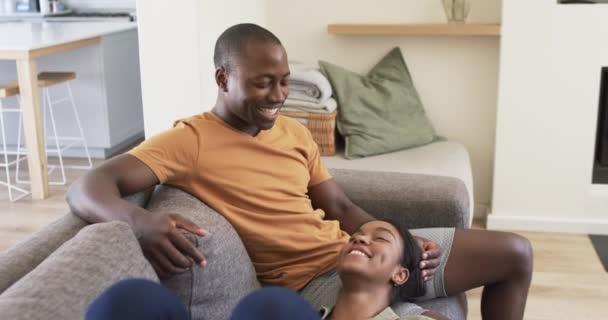 アフリカ系アメリカ人の若いカップルが家でリラックスし 暖かいトーンを通して 夫は短い髪型で 彼の妻に微笑み 彼女の頭は彼の膝の上に休んでいる 変更されていない — ストック動画