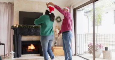 Noel zamanı, üst düzey Asyalı çift şöminenin önünde neşeyle dans ediyor, evde Noel Baba şapkaları takıyor, fotokopi çekiyor. Tatiller, kutlamalar, kış, Noel, yaşlılar, kutlamalar