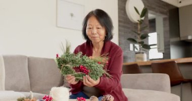 Gülümseyen kadın evde Noel çelengi yapıyor, yaratıcılığın tadını çıkarıyor. Tatil, dekorasyon, kutlama, DIY, mevsimlik, neşeli