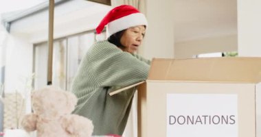 Noel Baba şapkalı yaşlı kadın Noel 'de eve oyuncak ayı bağışlıyor. Sadaka, bağış, bayram, cömertlik, son sınıf