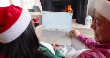 Noel zamanı, kıdemli Asyalı çift Noel Baba şapkası takıyor evde şöminenin yanında dizüstü bilgisayar kullanıyor, fotokopi çekiyor. Noel, şenlik, teknoloji, yaşlılar, kutlama, kış