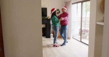 Noel zamanı, evde Noel Baba şapkası takan Asyalı bir çift şöminenin önünde neşeyle dans ediyor. Tatil, Noel, kutlama, şen, samimi, sıcak