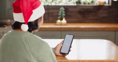 Son sınıf öğrencisi Noel 'de evde akıllı telefon kullanarak Noel Baba şapkası takıyor. Kopya odası. Yaşlılar, tatil, şenlik, teknoloji, iletişim, kış