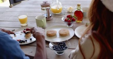 Noel zamanı, çeşitli çiftler gözleme ve açık havada taze meyvelerle neşeli bir kahvaltı yapıyorlar. Açık havada yemek, kutlama, sabah, birliktelik.