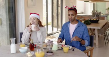 Çeşitli çiftler evde kahvaltıdan zevk alıyorlar, Noel şapkaları takıyorlar, gülümsüyorlar. Tatil, kutlama, aile, birliktelik, neşe, yemek.