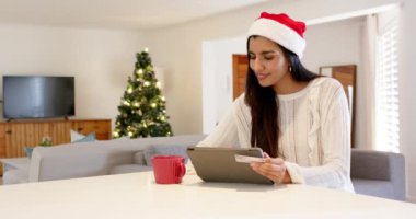 Noel zamanı, Noel Baba şapkalı Hintli kadın evde tabletle internetten alışveriş yapıyor. Tatil, Noel, online alışveriş, e-ticaret, şenlik, yaşam tarzı