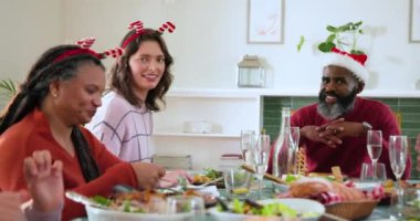Çeşitli aileler Noel yemeğini birlikte yiyor, tatil şapkaları takıyor ve gülümsüyor. Kutlama, tatil sezonu, toplanma, ziyafet, gelenek, birliktelik