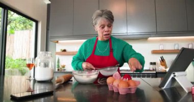 Noel 'de, kıdemli kadın mutfakta yemek pişiriyor, yumurta kırıyor ve neşeyle gülümsüyor. Yemek, mutluluk, yaşlılık, yaşam tarzı, aşçılık, hazırlık