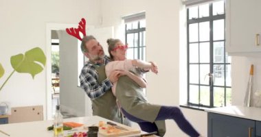 Noel 'de, yetişkin bir çift mutfakta neşeyle dans eder önlük giyer ve neşeli boynuzlar takar. Noel, tatil, kutlama, dans, mutluluk, aile