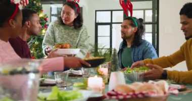 Noel yemeğini kutluyoruz, çeşitli arkadaşlar kızarmış tavuk paylaşıyor ve şenlik masasında gülüyorlar. Kutlama, tatil, yemek, toplanma, parti, eğlence