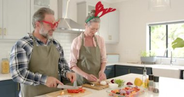 Noel 'de, neşeli çift mutfakta birlikte bayram yemeği hazırlıyor, ren geyiği boynuzları takıyorlar. Kutlama, yemek pişirme, birliktelik, aile, hazırlık