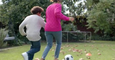 Mutlu Afro-Amerikan anne ve oğlu, futbol oynayıp bahçede yavaş çekimde kucaklaşıyorlar. Annelik, çocukluk, birliktelik, eğlence, sonbahar ve eğlence, değişmemiş.