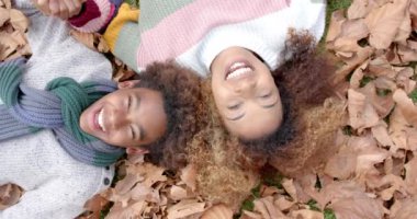 Mutlu Afro-Amerikan anne ve oğlu sıcak giysiler içinde bahçede düşen yaprakların üzerinde uzanıyorlar, ağır çekimde. Annelik, çocukluk, birliktelik, sonbahar ve rahatlık, değişmemiş.