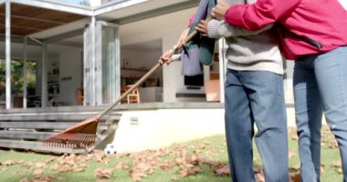 Mutlu Afro-Amerikan anne ve oğlu bahçede yaprakları yavaş çekimde tırmıklıyor. Annelik, çocukluk, birliktelik, sonbahar ve rahatlık, değişmemiş.