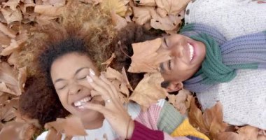 Mutlu Afro-Amerikan anne ve oğlu sıcak giysiler içinde bahçede düşen yaprakların üzerinde uzanıyorlar, ağır çekimde. Annelik, çocukluk, birliktelik, sonbahar ve rahatlık, değişmemiş.