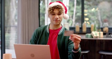 Noel Baba şapkalı Asyalı adam evde dizüstü bilgisayar kullanıyor. tatil, festival, teknoloji, online, kutlama, gelenek