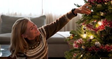 Kıdemli kadın evde Noel ağacı süslemenin tadını çıkarıyor. Tatil, kutlama, aile, dekorasyon, yaşlılık, gelenek