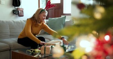 Gülümseyen kadın evde Noel hediyelerini paketliyor, rengeyiği saç bandı takıyor. Tatil, kutlama, gelenek, hediye verme, kış, neşe