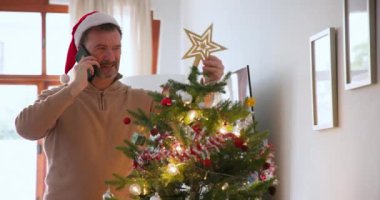 Evde akıllı telefonla konuşurken Noel ağacını süsleyen son sınıf öğrencisi. Tatil, festival, kutlama, yaşlılar, iletişim, teknoloji