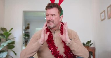 Ren geyiği boynuzu takan ve Noel 'i evde kutlayan kıdemli bir adam. Tatil, şenlik, kutlama, neşe, dekorasyon, konfor