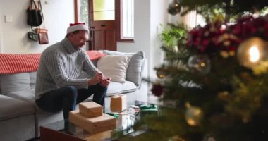 Kıdemli adam evde Noel hediyelerini paketliyor, süslenmiş ağacın yanında gülümsüyor. bayram, hediye, bayram, gelenek, kış, kutlama