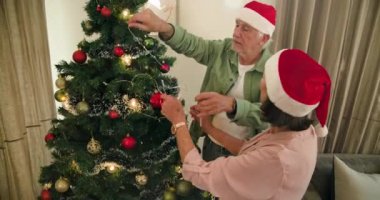 Noel ağacını evde süsleyen, Noel Baba şapkası takan yaşlı çift. Kutlama, tatil, yaşlılar, gelenek, şenlik ruhu, birliktelik