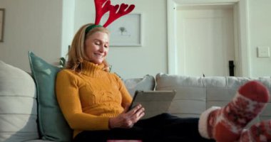 Noel 'de, evde dinlenirken ren geyiği boynuzları takan yaşlı bir kadın sıcak içkinin tadını çıkarıyor. Rahatlama, şenlik, tatil, rahat, yaşlı, boş zaman