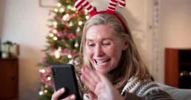Akıllı telefonlu gülümseyen kadın Noel 'in tadını çıkarıyor evde süslü ağacın yanında. Tatil, kutlama, şenlik, dekorasyon, Noel ağacı, kış