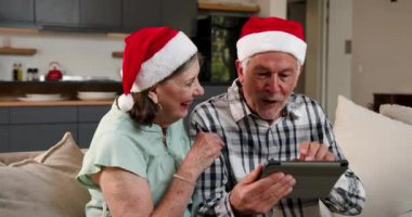 Noel Baba şapkası takan yaşlı çift evde tablet kullanıyor, birlikte Noel 'in tadını çıkarıyorlar. Tatiller, festival, teknoloji, aile, kutlama, yaşlılar