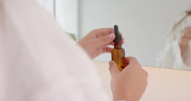 Düşürme şişesi kullanan, banyodaki ayna yansımasına cilt serumu uygulayan kadın. güzellik, bakım, kozmetik, rutin, kişisel bakım, sağlık