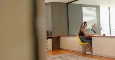 Evden çalışan, dizüstü bilgisayar kullanan ve modern ofiste kahve fincanı tutan bir kadın. Uzaktan çalışma, ev ofisi, verimlilik, telekomünikasyon, teknoloji, gündelik