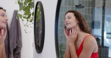 Cilt bakımı, aynaya bakan ve banyoda yüzüne dokunan bir kadın. Güzellik, kendine bakım, rutin, kozmetik, sağlık, bakım