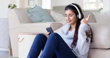 Evde dinlenen, kulaklıkla müzik dinleyen akıllı telefonlu bir kadın. Boş zaman, rahatlama, teknoloji, yaşam tarzı, eğlence