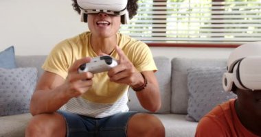 VR kulaklıklarıyla video oyunları oynuyorlar, iki çok ırklı erkek arkadaş evde eğleniyorlar. Teknoloji, oyun, sanal gerçeklik, eğlence, arkadaşlık, eğlence