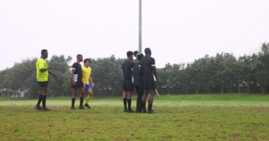 Futbol oynamak, takım halinde sahada toplanmak maç sırasında strateji tartışmak. Spor, takım çalışması, rekabet, birlik, açık hava, takım ruhu.