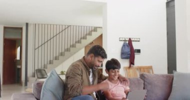 Hintli baba ve oğul kanepede oturup tablet kullanıyor, bağ kuruyor ve birlikte öğreniyorlar. Aile, teknoloji, ebeveynlik, ev, eğitim