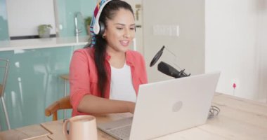 Podcast kaydı, dizüstü bilgisayar ve mikrofon kullanan Asyalı bir kadın, kulaklık takıyor, gülümsüyor, evde. Podcasting, teknoloji, ses, yayın, iletişim, iş istasyonu