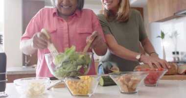 Salata hazırlıyorum, çok ırklı son sınıf bayan arkadaşlar modern mutfakta, evde eğleniyorlar. Yemek, sağlıklı beslenme, arkadaşlık, yaşam tarzı, ev, beslenme