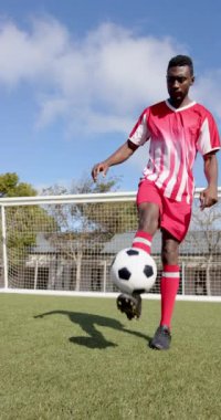 Dikey video: Kırmızı üniformalı futbolcu sahada ustalıkla top oynuyor. Sporcu, spor, futbol, beceri, rekabet, eğlence