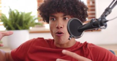 Gülümseyen genç adam mikrofona konuşuyor, podcast 'i evde kaydediyor. Yayın, ses, teknoloji, iletişim, ev stüdyosu, içerik oluşturma