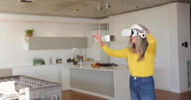VR kulaklık kullanan bir kadın modern mutfakta sanal çevreyle etkileşime geçiyor. Evinde, kopyalama alanında. Teknoloji, yenilik, sanal gerçeklik, sürükleyici, akıllı ev, etkileşim