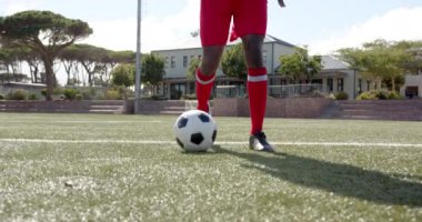 Sahada futbol oynayan, kırmızı üniformalı Afro-Amerikan erkek sporcu maç sırasında top sürüyor. Spor, rekabet, aksiyon, takım çalışması, açık hava