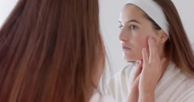 Aynaya bakan, cildini muayene eden ve kaplıcada yüzüne dokunan bir kadın. Cilt bakımı, sağlık, güzellik, özbakım, yansıma, rutin