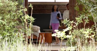 Bahçede gülümseyen ve sohbet eden yoga minderleri olan iki çok ırklı bayan arkadaş. Sağlık, dostluk, rahatlama, egzersiz, veranda, yaşam tarzı